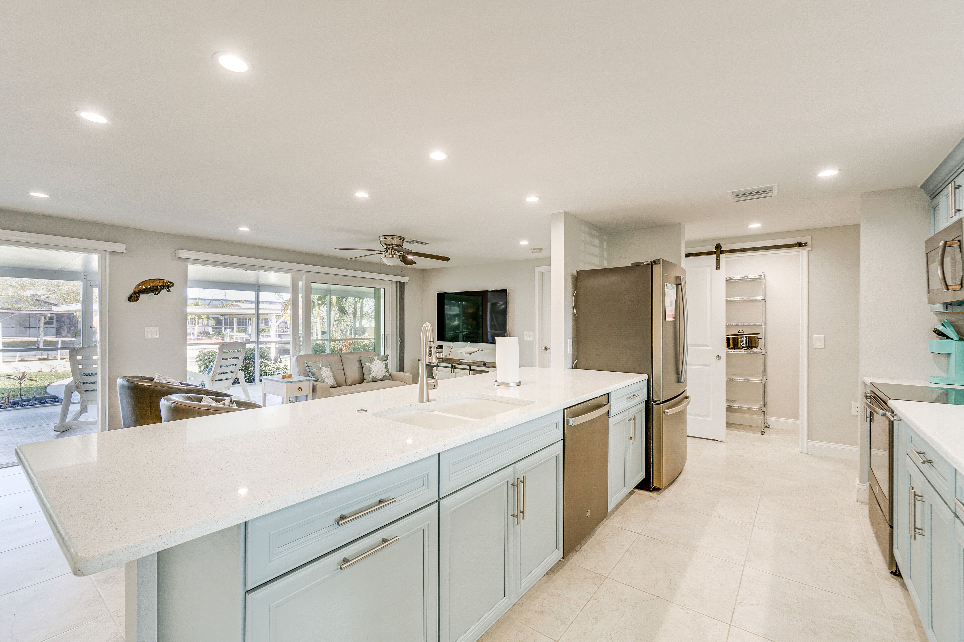 A modern kitchen with a large island, stainless steel appliances, and a sliding door leading to a pantry.