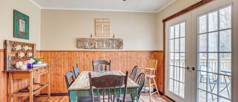 A dining area with a wooden table and chairs, a ceiling fan, and a large window with a view of the outdoors.