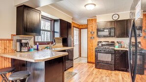 A kitchen with dark wooden cabinets, a central island with stools, a microwave, stove, and refrigerator. - Hayward Home w/ Private Deck, Fire Pit & Kayak! (Hayward)