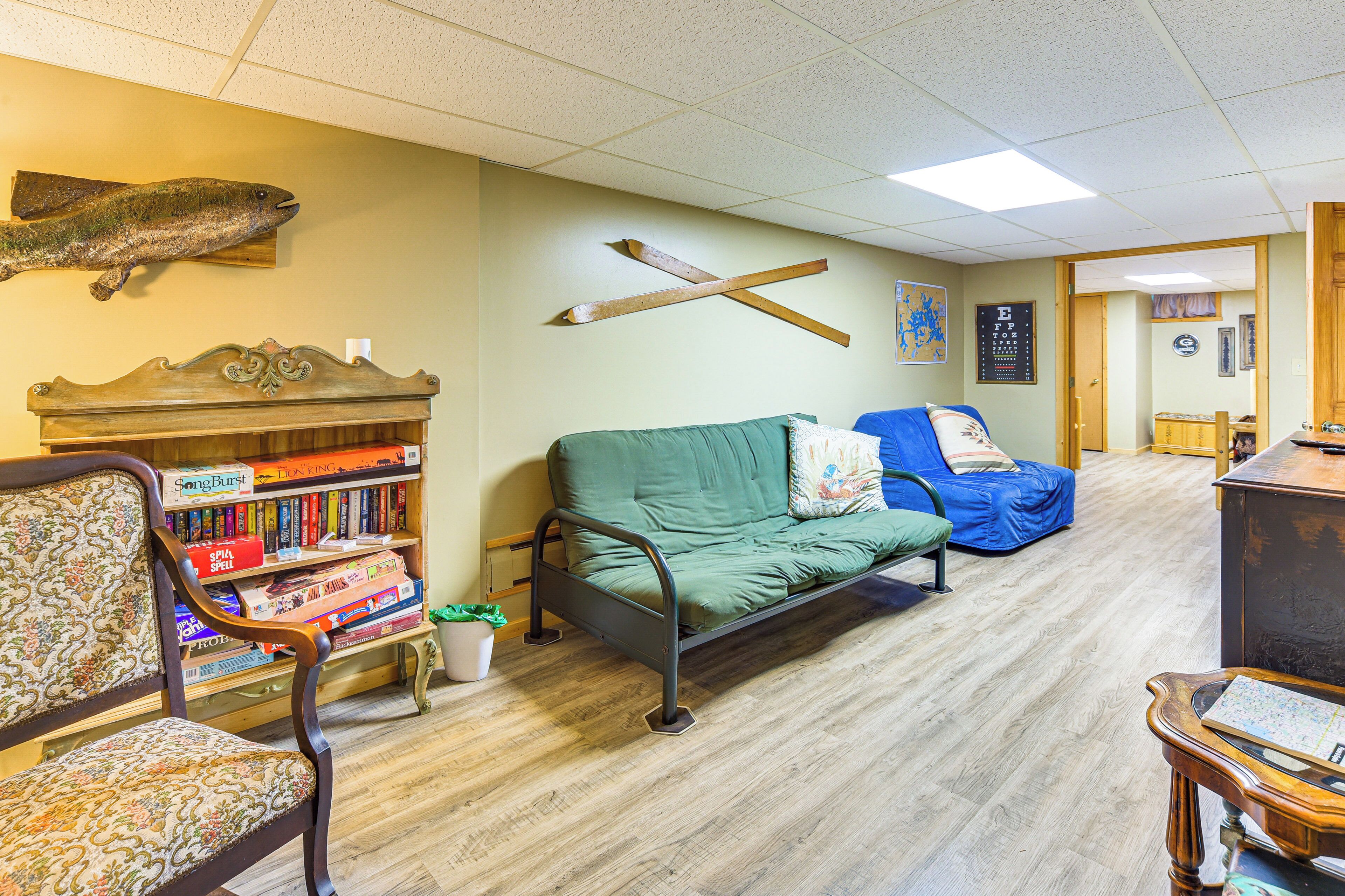 A cozy room with a green sofa, a wooden bookshelf, a decorative fish on the wall, and a wooden desk.
