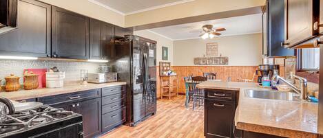 A modern kitchen with dark cabinets, a stainless steel refrigerator, a gas stove, and a wooden floor.