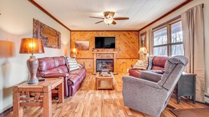 A cozy living room with a fireplace, leather sofas, a wooden coffee table, and a ceiling fan. - Hayward Home w/ Private Deck, Fire Pit & Kayak! (Hayward)