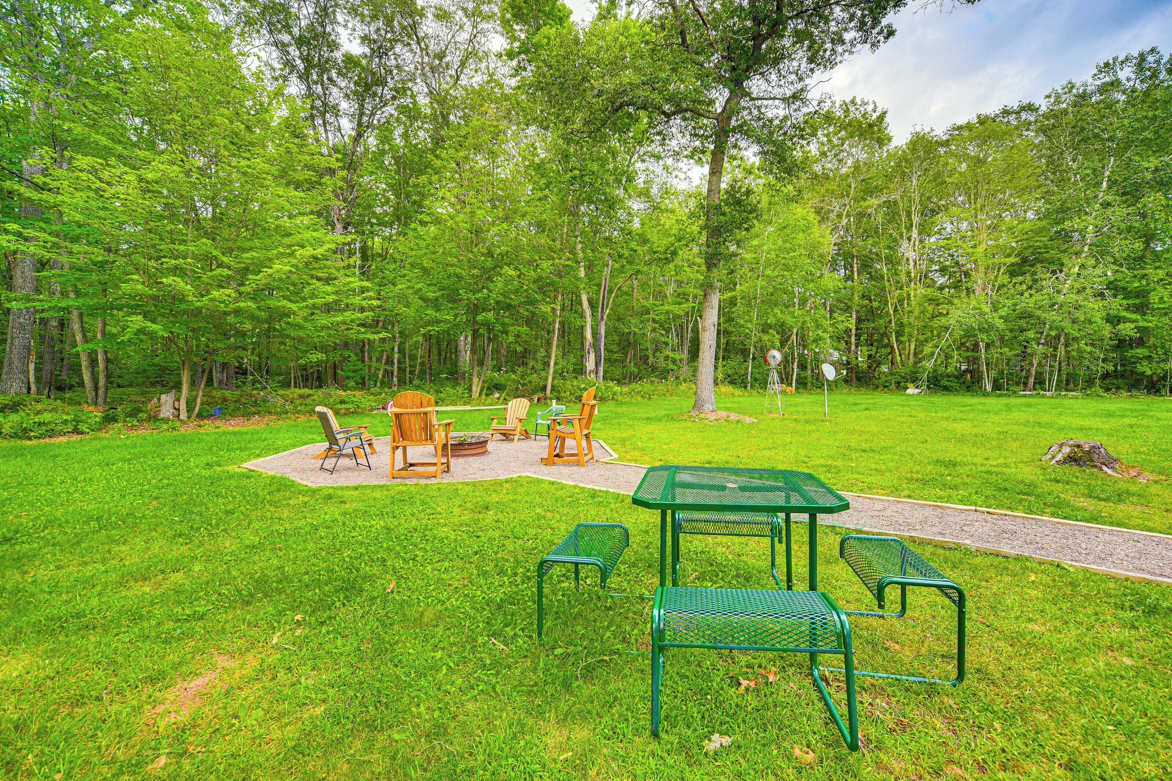 Een park met een picknickplaats, met groene metalen tafels en stoelen, omringd door weelderige groene bomen.