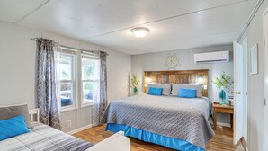 Ein Schlafzimmer mit einem großen Bett, einem kleineren Bett, einem Nachttisch, einem Fenster mit Vorhängen und einer Klimaanlage.