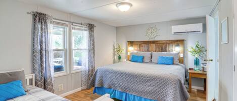 A bedroom with a large bed, a smaller bed, a nightstand, a window with curtains, and an air conditioning unit.