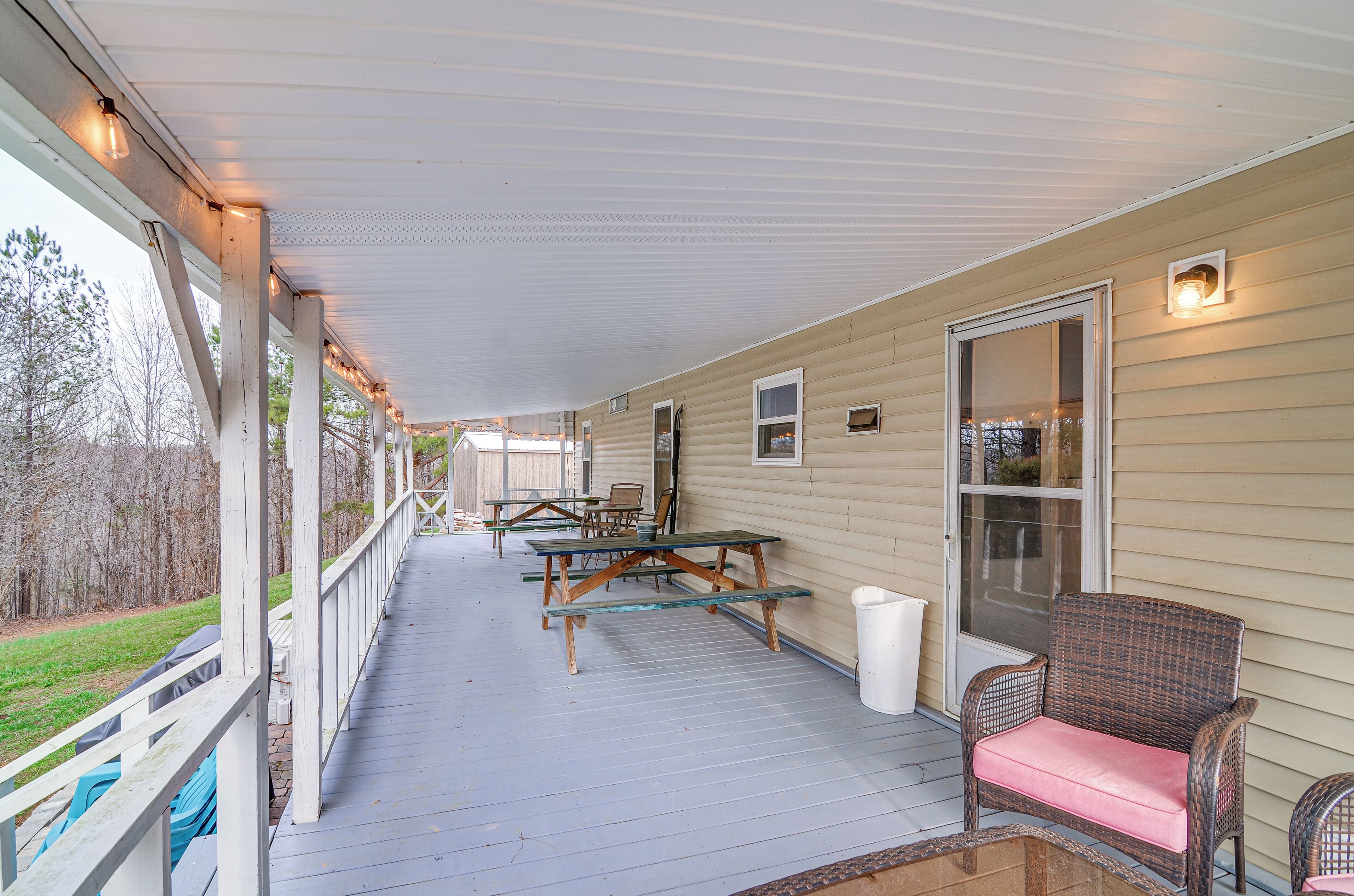 A covered porch with picnic tables and chairs, a door with a glass panel, and a railing.