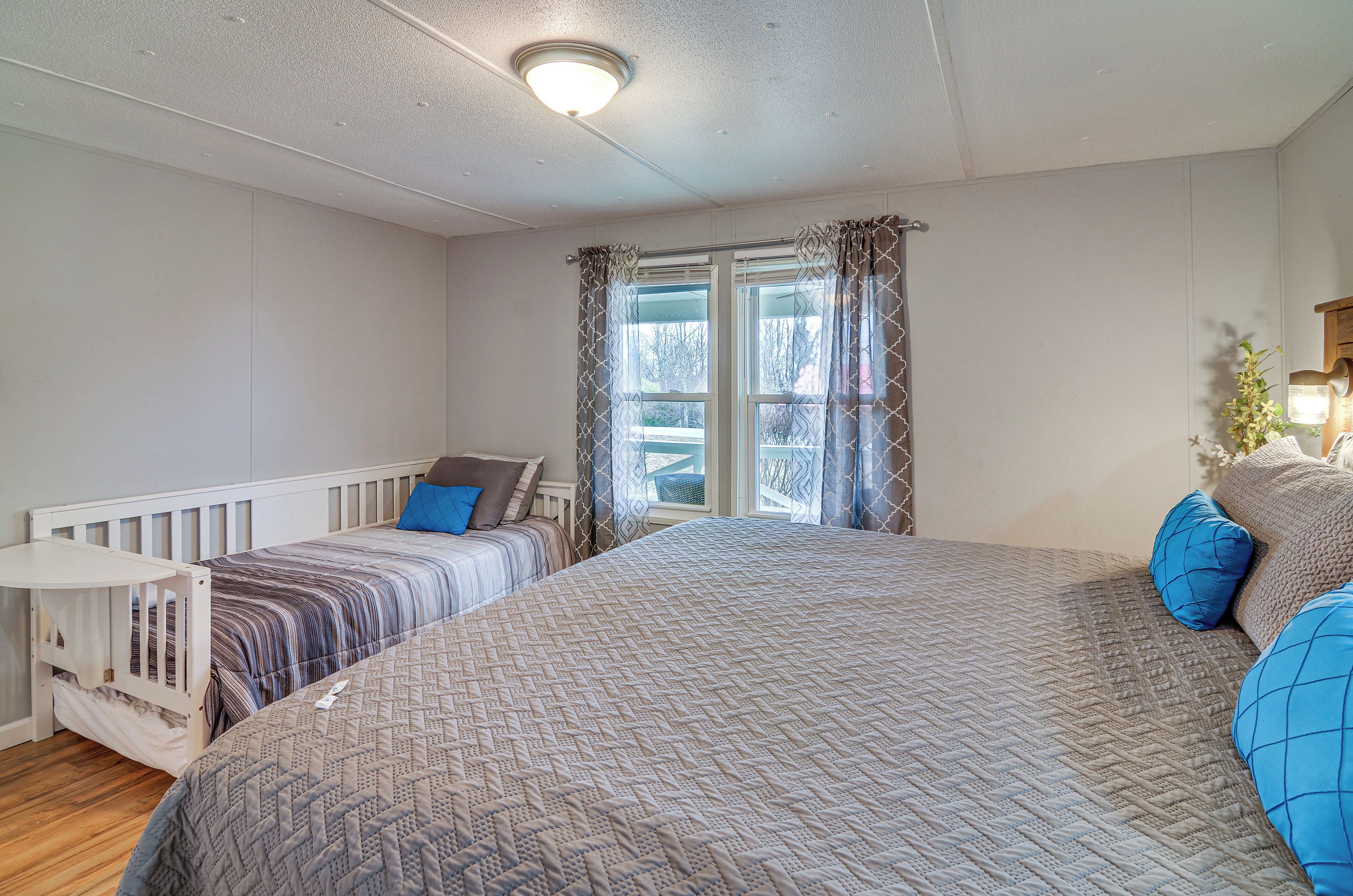 Un dormitorio con una cama grande, una cama más pequeña, una cuna y una ventana con cortinas.