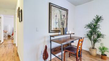 A dining area with a wooden table, two chairs, a framed painting, and two potted plants.