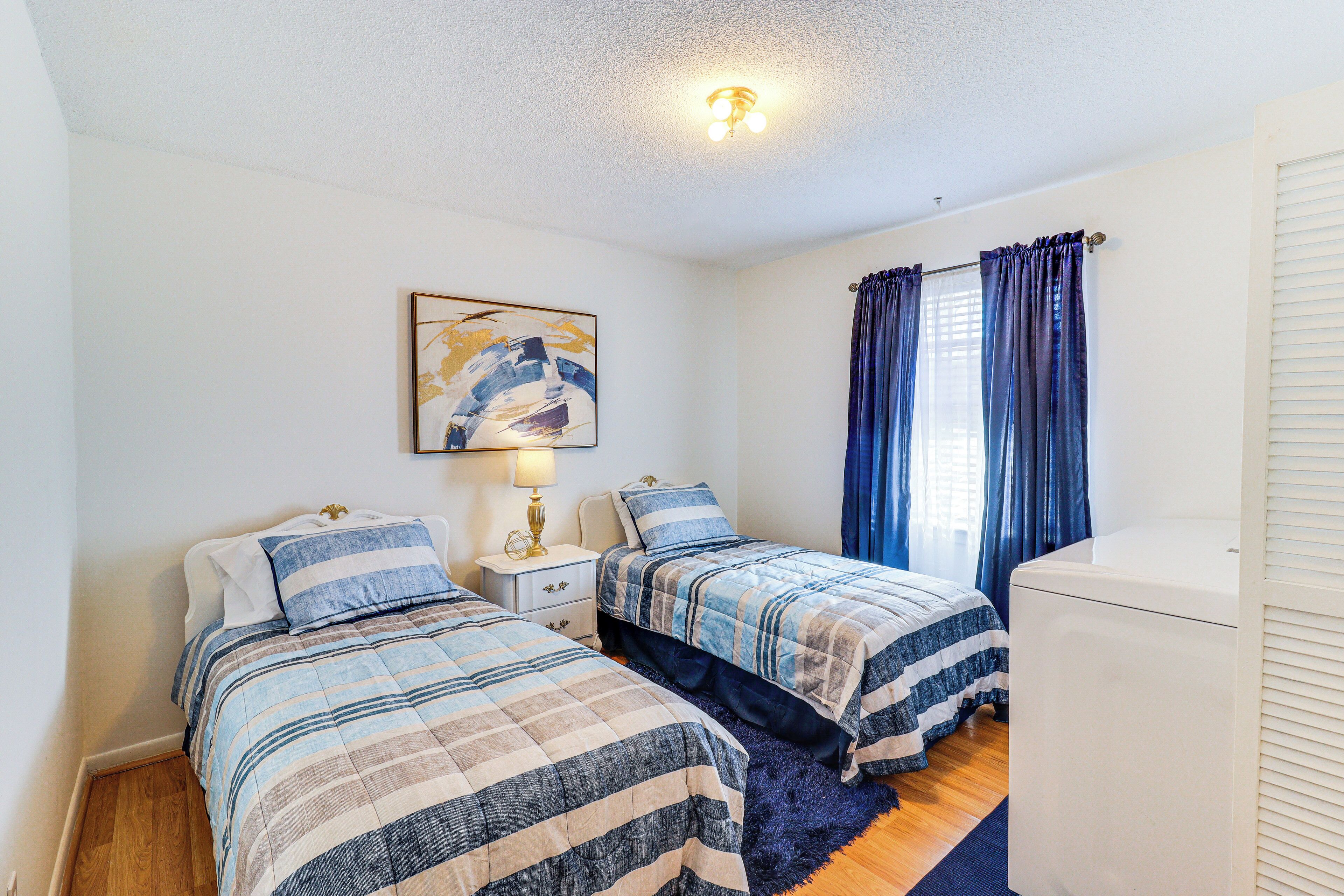 A bedroom with two beds, a nightstand, a lamp, a window with curtains, and a ceiling light.
