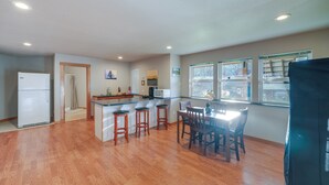 A spacious kitchen with wooden flooring, a central island with stools, a dining table with chairs, and a refrigerator. - Quaint Mount Vernon Studio Rental w/ Big Lake View (Mount Vernon)