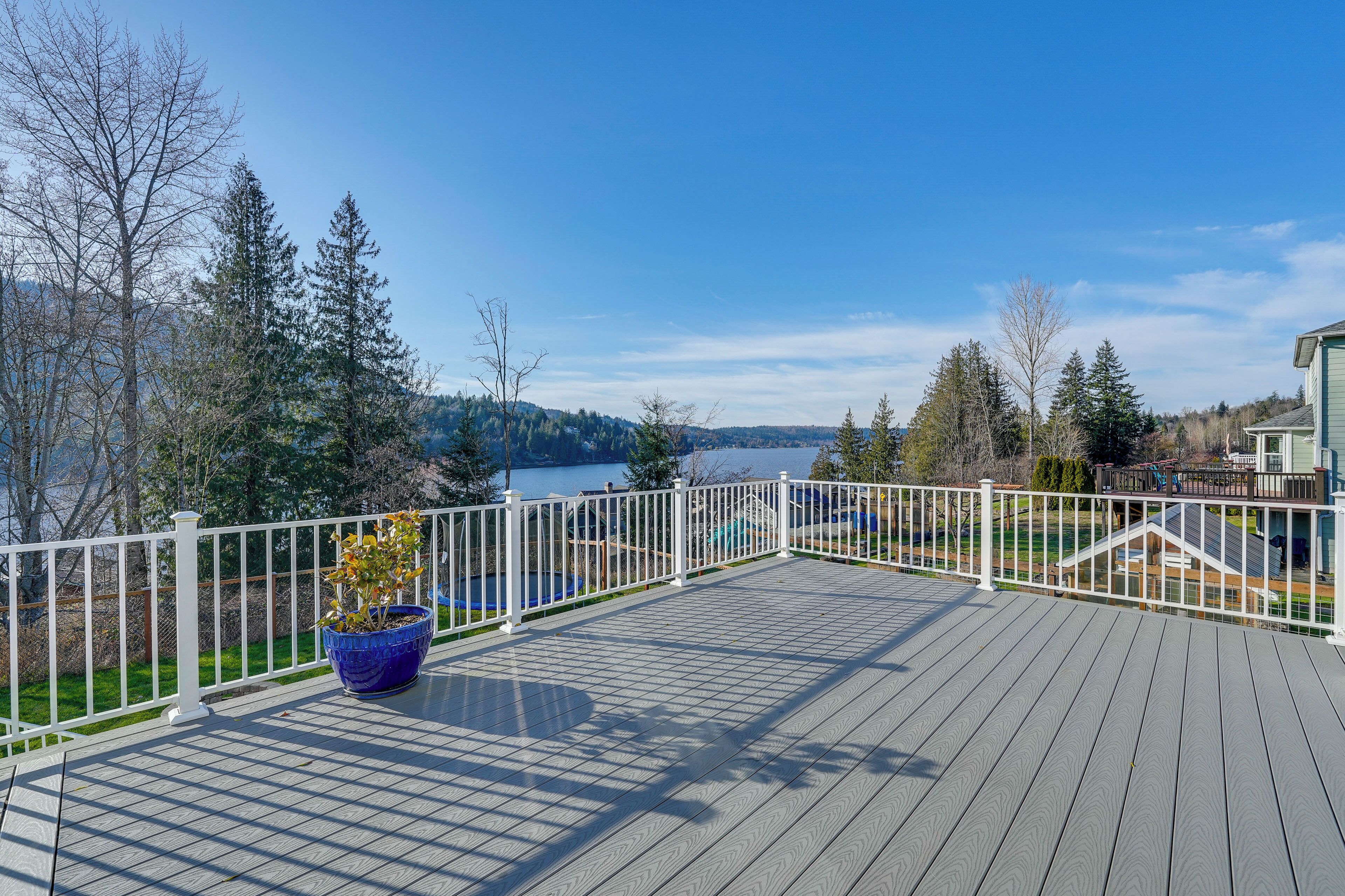 Une terrasse en bois avec une balustrade blanche, donnant sur un lac et des arbres.