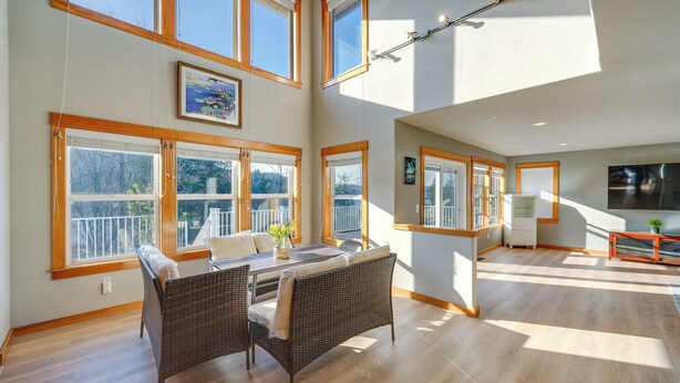 A spacious living area with a dining table, wicker furniture, and large windows offering views of a balcony and trees. - Stunning Mount Vernon Home w/ Big Lake Views! (Mount Vernon)