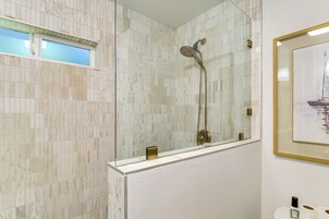 Un baño con cabina de ducha de vidrio, una bañera blanca y un cuadro en la pared.