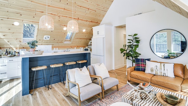 Una cocina moderna con una isla central, taburetes de bar y una zona de estar con sofá y sillones.