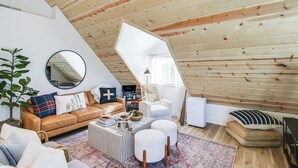 Acogedor loft con techo inclinado, un espejo redondo, sofá de cuero, una mesa de centro y un sillón blanco.