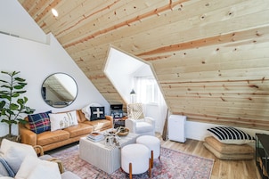 Acogedor loft con techo inclinado, un espejo redondo, sofá de cuero, una mesa de centro y un sillón blanco.