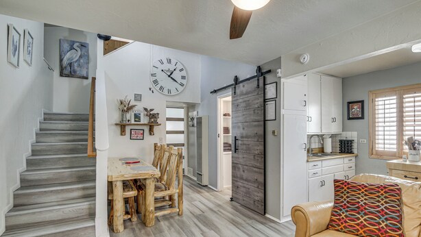 A modern kitchen with a large clock, a dining area with a wooden table and chairs, and a staircase leading to another level. - Cozy Cabin w/ Deck - 2 Mi to Bear Mountain Resort! (Big Bear Lake)