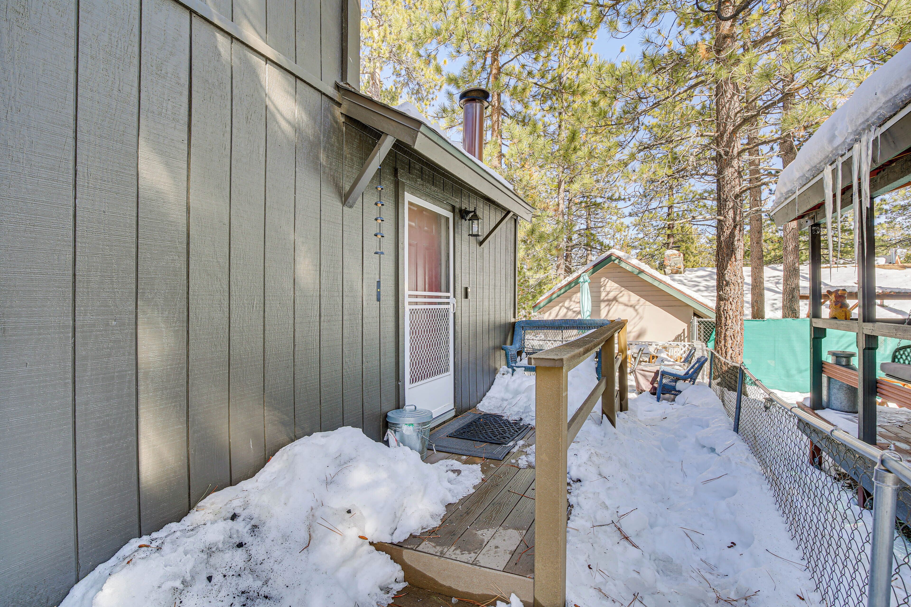 A wooden cabin with a metal fence, a wooden deck, and a snow-covered ground.