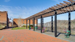 A covered outdoor area with a brick pathway, wooden pergola, and colorful folding chairs. - Downtown Lynchburg Condo w/ James River Views (Lynchburg)