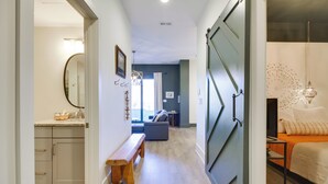 A hallway with a bench, a dining area with a table and chairs, and a bedroom with a bed and a nightstand. - Downtown Lynchburg Condo w/ James River Views (Lynchburg)