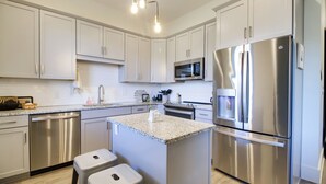 A modern kitchen with stainless steel appliances, white cabinetry, and a granite countertop island with stools. - Downtown Lynchburg Condo w/ James River Views (Lynchburg)