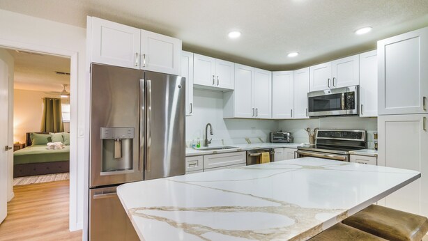 A modern kitchen with white cabinets, stainless steel appliances, and a marble countertop. - Home w/ Screened Porch, Near Weeki Wachee Springs! (Spring Hill)