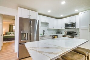 A modern kitchen with white cabinets, stainless steel appliances, and a marble countertop.