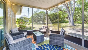 A covered patio with wicker furniture, large windows, and a view of trees and grass. - Home w/ Screened Porch, Near Weeki Wachee Springs! (Spring Hill)