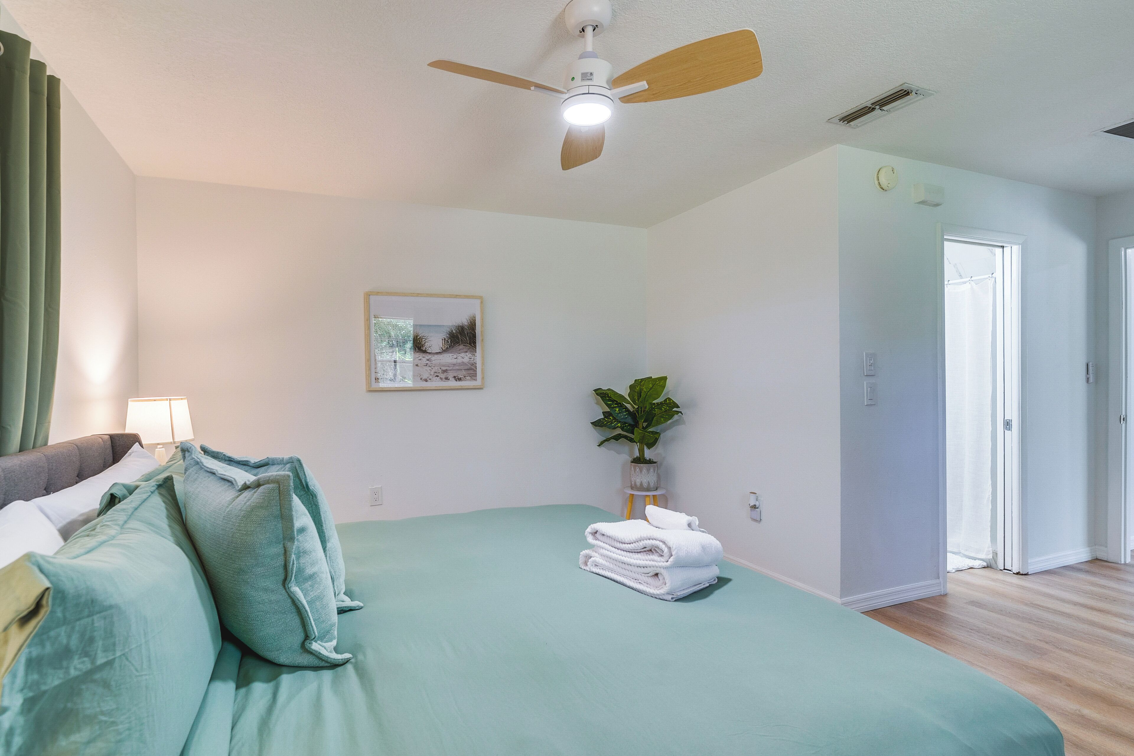 A bedroom with a bed, a ceiling fan, a potted plant, and a framed picture on the wall.