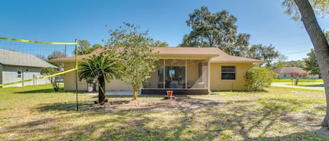 A single-story house with a front porch, a small tree, and a volleyball net in the yard.