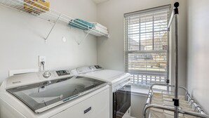 Un espace buanderie équipé d’un lave-linge et d’un sèche-linge Maytag, d’un étendoir et d’une fenêtre avec des stores.