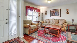 Un salon comprenant un canapé, un fauteuil et une table basse, ainsi qu’un tapis à motifs et un tableau accroché au mur.