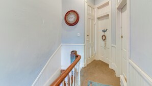 Un pasillo con escaleras de madera, puertas blancas y un reloj de pared.