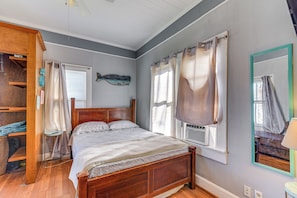 A bedroom with a wooden bed, a small bedside table, a wall-mounted heater, and a window with curtains.
