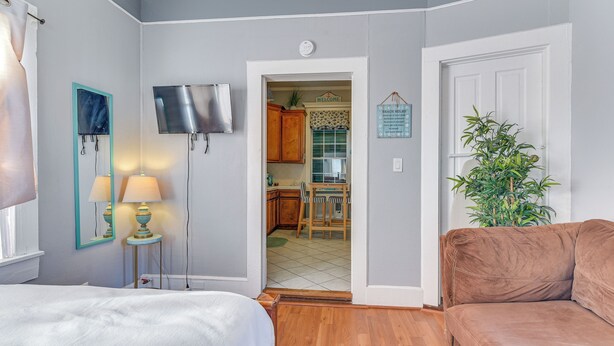 Un dormitorio con cama, lámparas de noche, televisor y una puerta que da a la cocina.