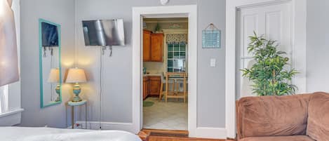 Une chambre à coucher comprenant un lit, des lampes de chevet, une télévision et une porte donnant sur la cuisine.