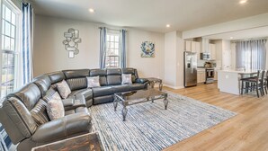 A modern living room with a sectional sofa, a coffee table, and a kitchen in the background. - 30 Mi to Downtown DC: Charming Dale City Townhome! (Woodbridge)