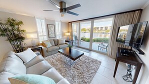 A modern living room with a sofa, coffee table, and TV. There is a large window with a view of buildings and a body of water. - Dolphin Point 105b 2 Bedroom Condo by RedAwning (Destin)