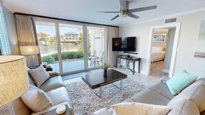 A modern hotel room with a large sliding glass door leading to a pool area, a flat-screen TV, a sofa, and a coffee table. - Dolphin Point 105b 2 Bedroom Condo by RedAwning (Destin)