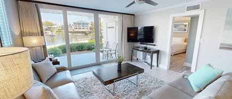 Quarto de hotel moderno com uma grande porta de vidro deslizante que dá para uma área de piscina, televisão de tela plana, um sofá e uma mesa de centro.