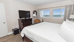 Un dormitorio con una cama grande, televisión, cómoda y vista al océano.