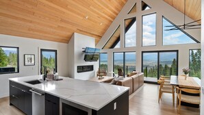 A modern kitchen with a large island, a dining area with a wooden table, and large windows offering scenic views. - Mountain Vista 3 Bedroom Chalet by RedAwning (Tabernash)