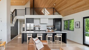 A modern kitchen with a central island, bar stools, and a mezzanine level with a railing. - Mountain Vista 3 Bedroom Chalet by RedAwning (Tabernash)