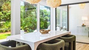Un comedor moderno con una mesa blanca, sillas tapizadas en verde y vistas a un follaje exuberante.