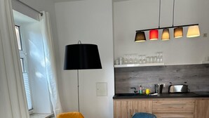 Et moderne køkken med en central ø, et spiseområde med et glasbord og stole, samt et hængende lysarmatur over bordet.