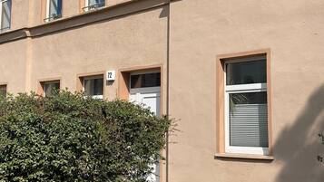 Ein mehrstöckiges Gebäude mit einer beigefarbenen Fassade, zahlreichen Fenstern und einer kleinen Grünfläche davor.