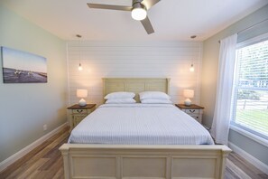 A bedroom with a bed, two bedside tables, a ceiling fan, and a window with curtains. - Stunning-waterfront, beach, pools, family fun (Long Neck)