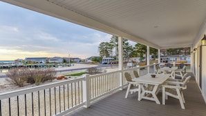 A covered outdoor deck with white railings and tables, overlooking a beach and houses.