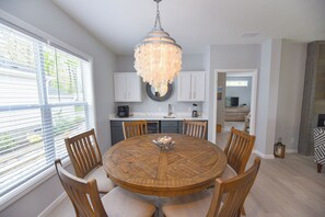 A dining area with a round wooden table, six chairs, and a central chandelier.