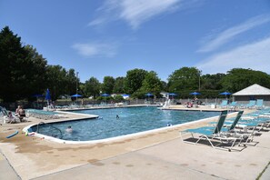 A swimming pool area with multiple pools, lounge chairs, and umbrellas.